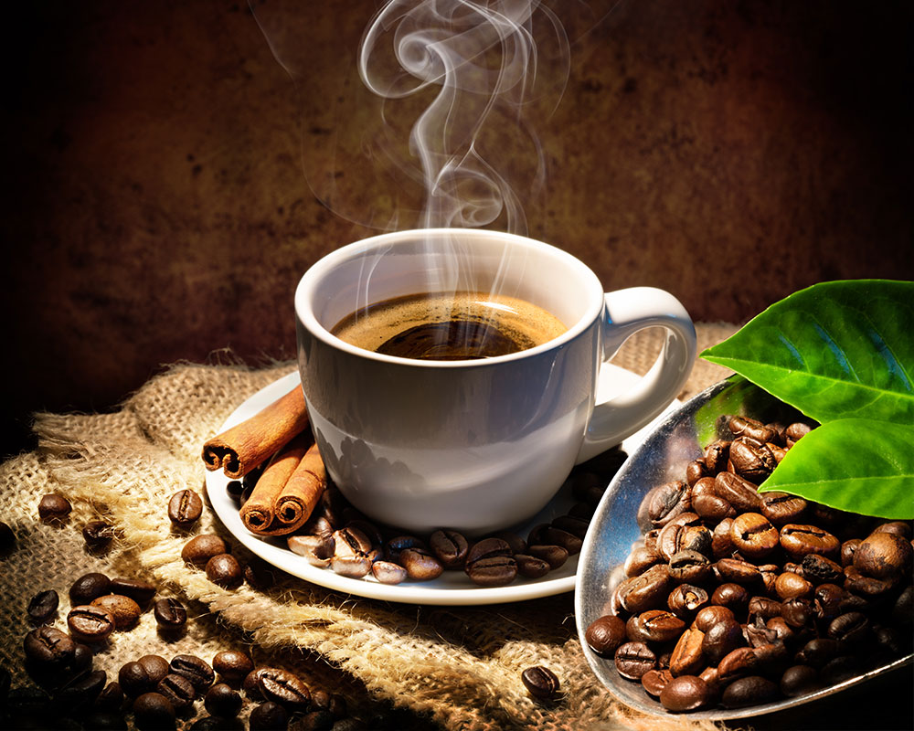Coffee cup with steam and cinnamon surrounded by coffee beans